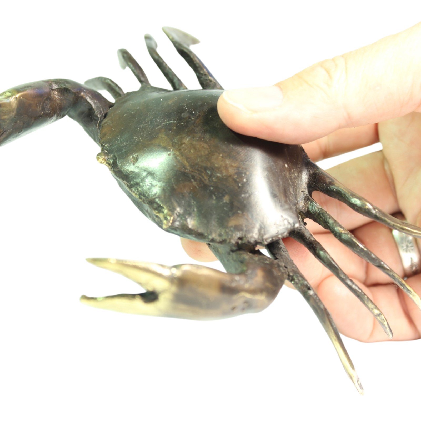 Back view of brass crab figurine held in hand with claws extended forward