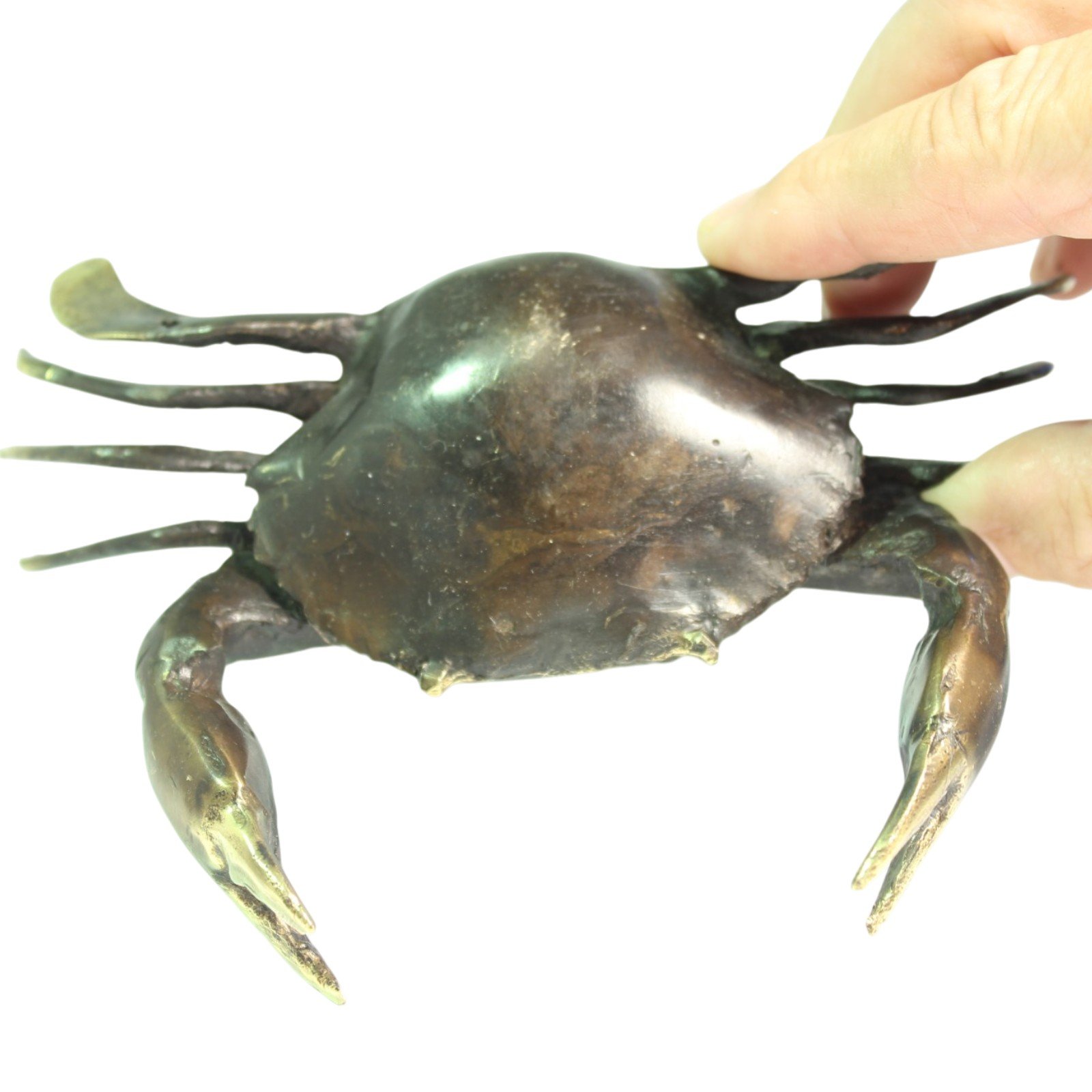 Underside view of brass crab held between fingers, showing legs and casting texture