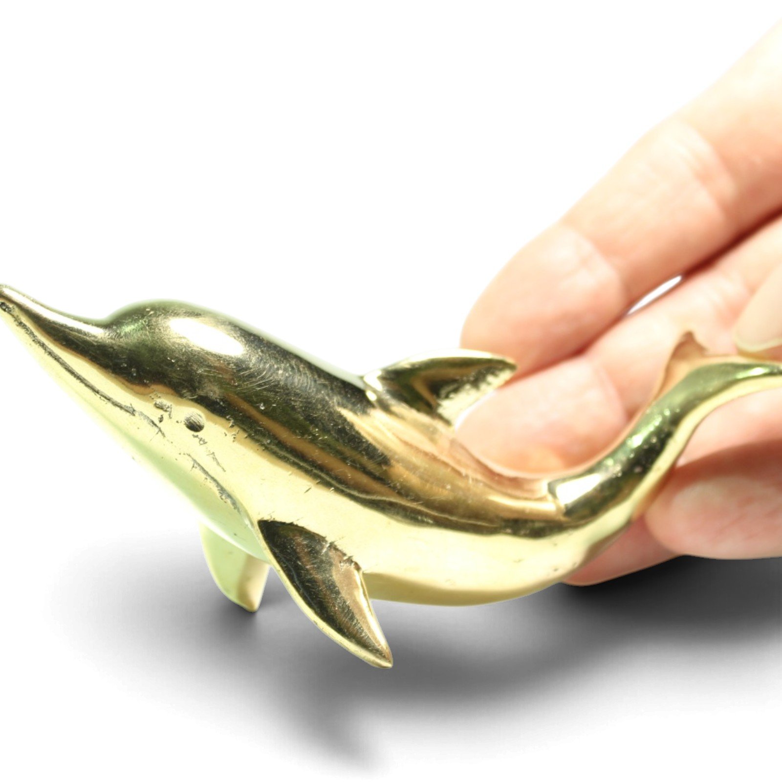 Close-up of a hand holding the brass dolphin figurine, showing scale