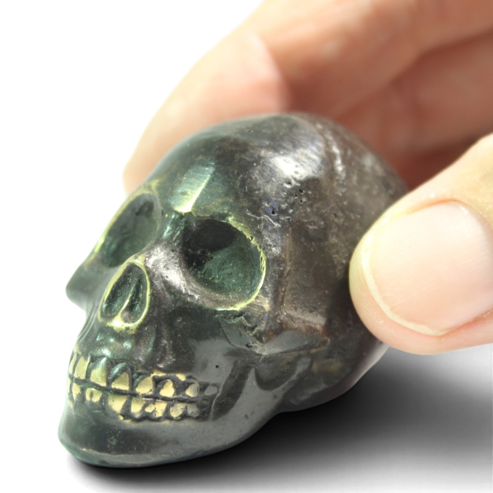 Close-up of fingers holding the brass skull, showing teeth and nose detail