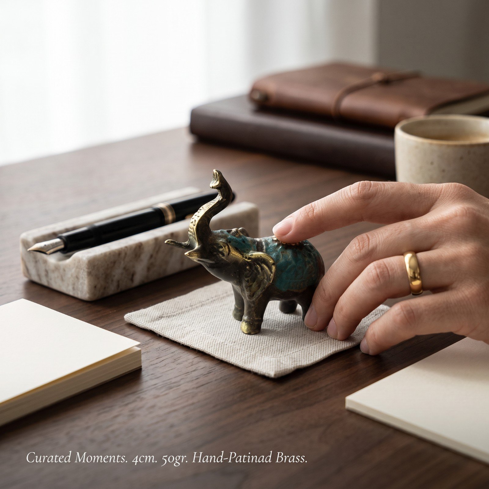 Hand holding the brass elephant figurine on a desk styled with a notebook and pen