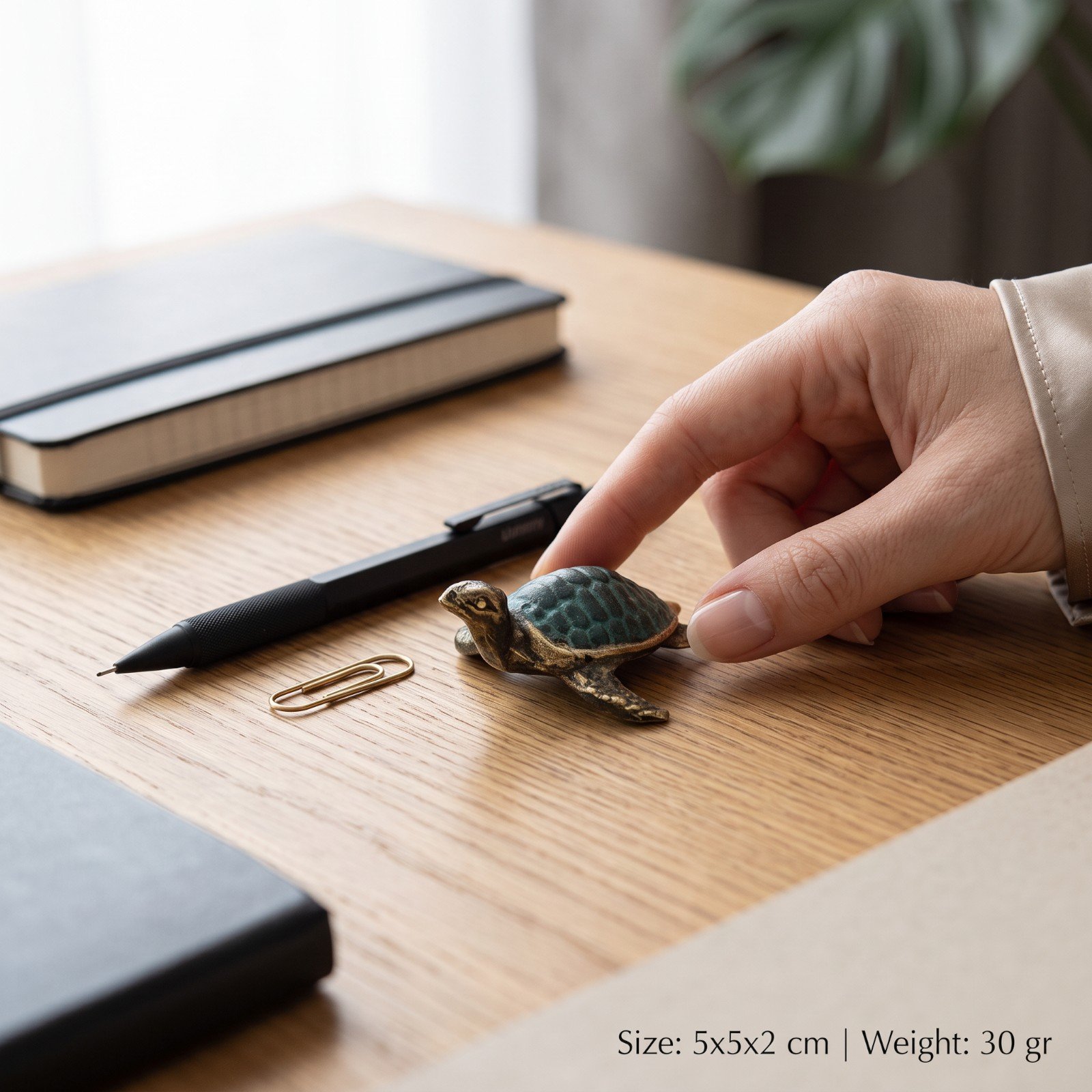 Brass turtle figurine staged on a desk beside a pen and paperclip with size reference
