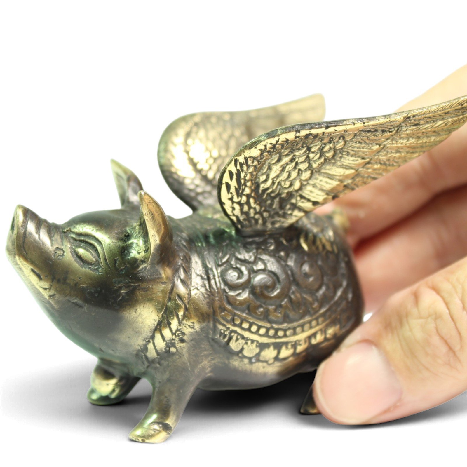 Close-up of hand holding the brass pig, showing wing texture and patina detail