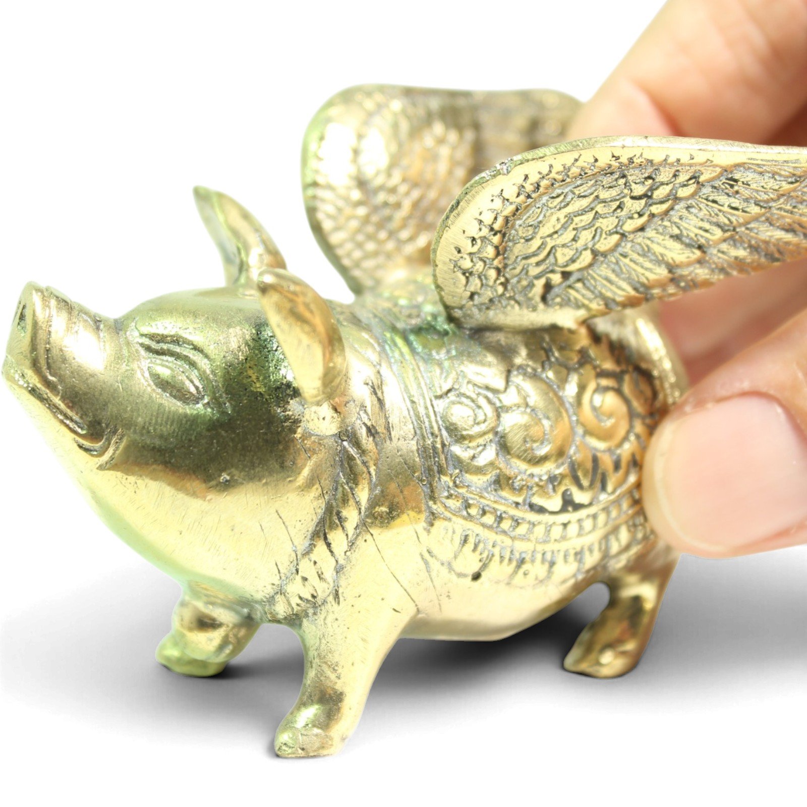 Brass winged pig figurine viewed from the side, showing detailed feathered wings and engraved saddle pattern
