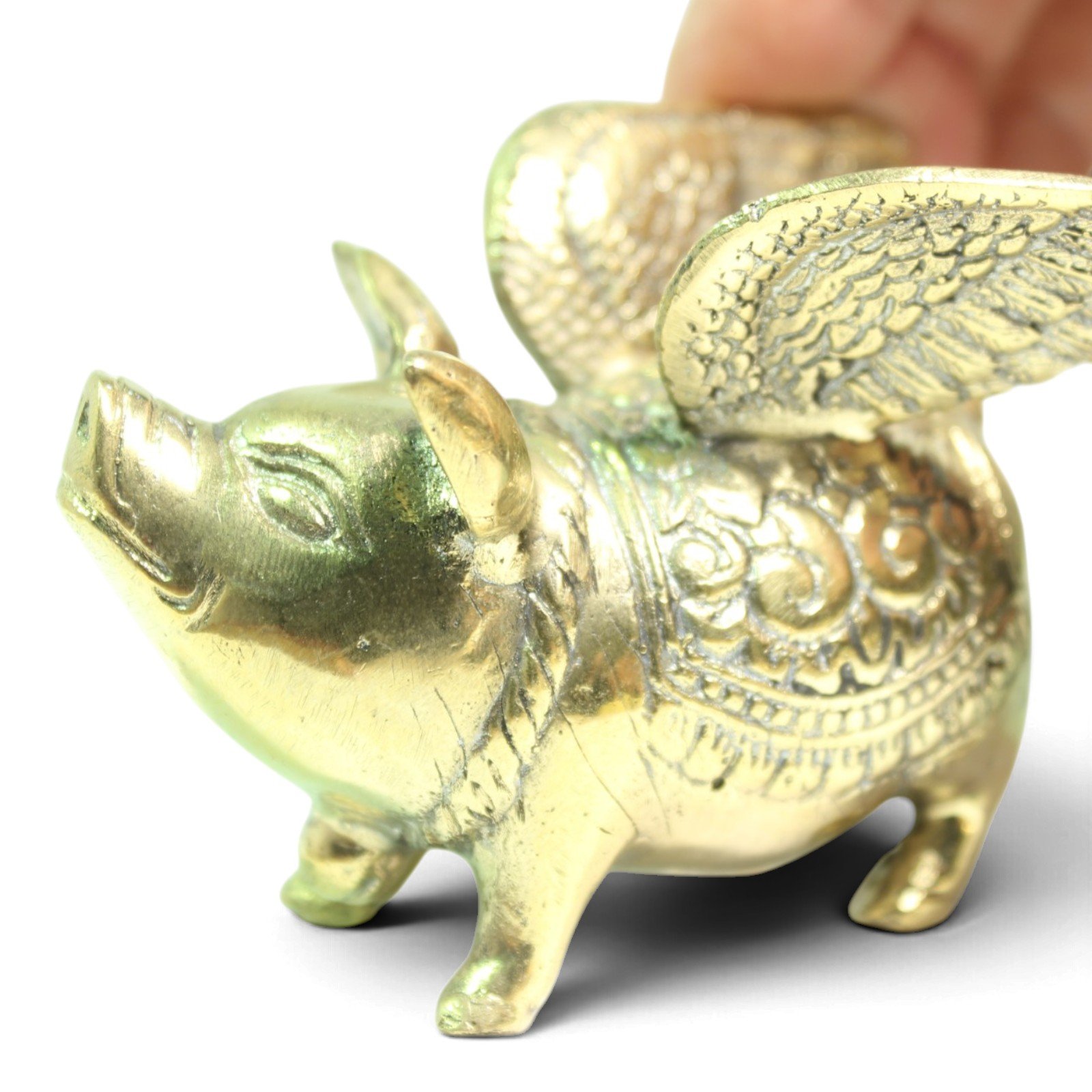 Brass winged pig figurine viewed from the side, showing detailed feathered wings and engraved saddle pattern