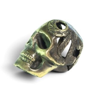 Small brass skull figurine with carved feathered headdress, shown at an angle against a white background