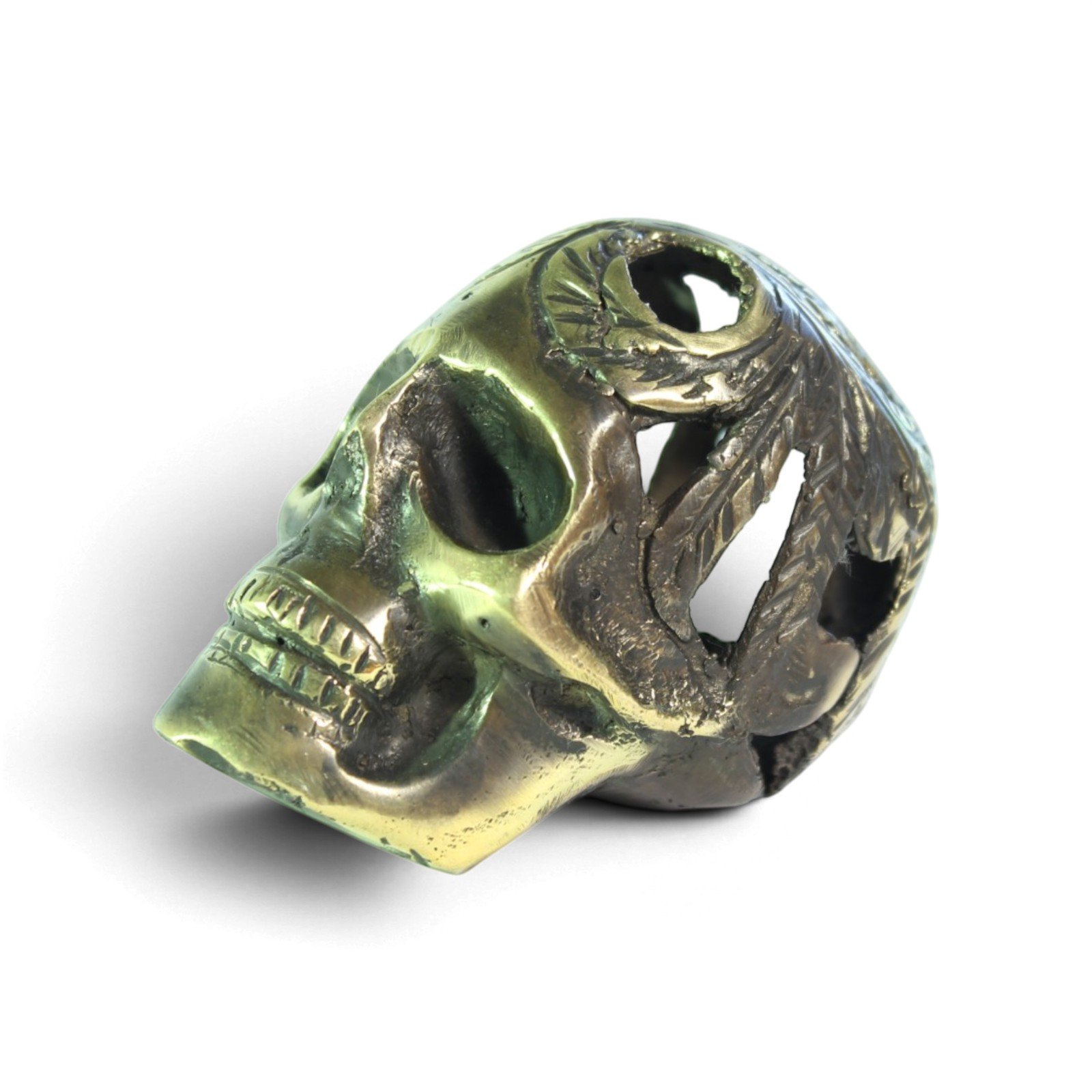 Small brass skull figurine with carved feathered headdress, shown at an angle against a white background
